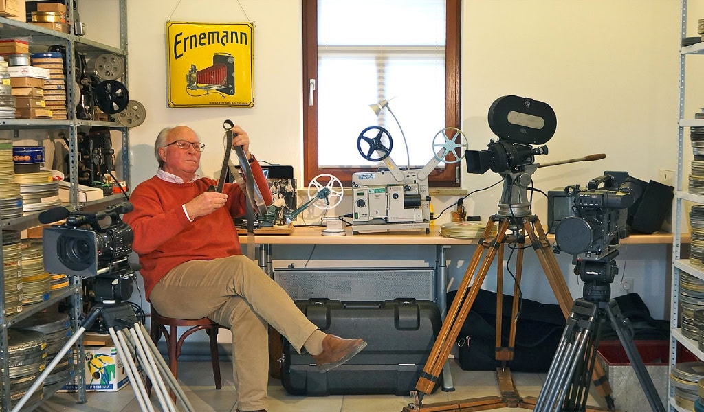 Arbeitsraum mit alten Filmkameras, Projektor und Filmrollen im Archiv, historische Filmtechnik. Ganz links sitzt der Dresdner Regisseur Ernst Hirsch.