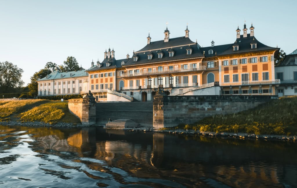 Das Wasserpalais von Schloss Pillnitz in Dresden wird von der tief stehenden Abendsonne angestrahlt. Eine breite Freitreppe führt vom Schloss zur Elbe.