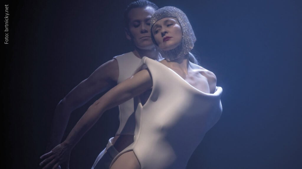 anzpaar in weiß mit glitzernder Kopfbedeckung auf dunkler Bühne