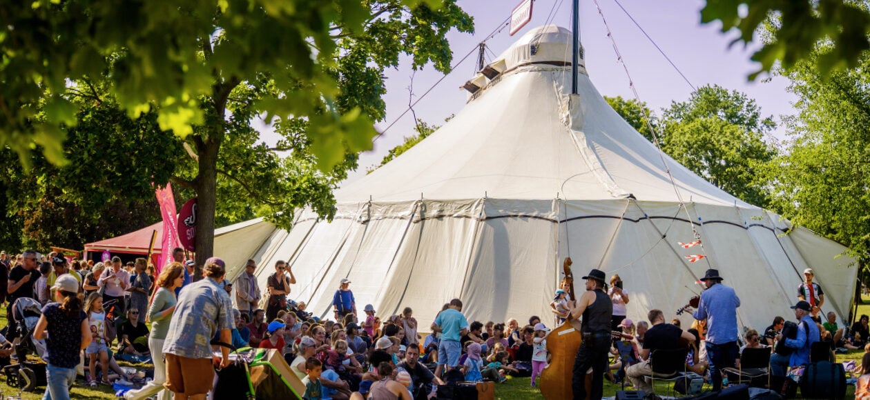 Zirkustheater-Festival Dresden 2026: Eine Menschenansammlung steht und sitzt vor einem Zirkuszelt.