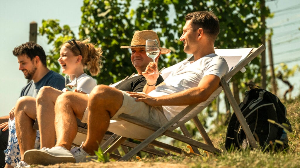 Menschen sitzen Im Liegestuhl und trinken ein Glas Wein. Und sitzen auf Liegestühlen am Weinhang.