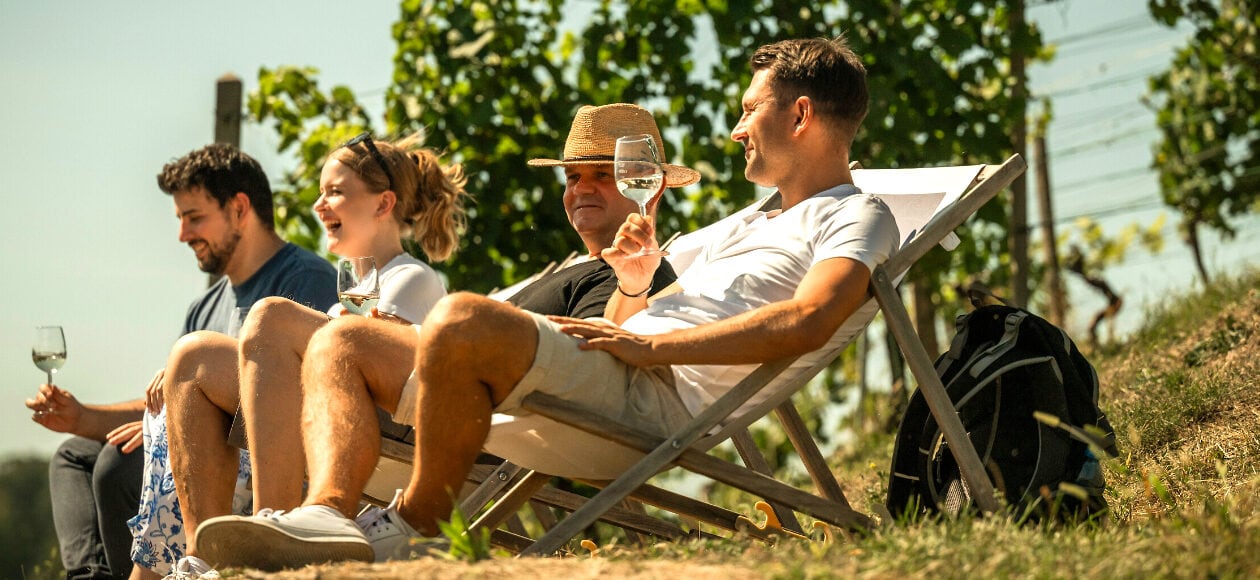 Menschen sitzen Im Liegestuhl und trinken ein Glas Wein. Und sitzen auf Liegestühlen am Weinhang.