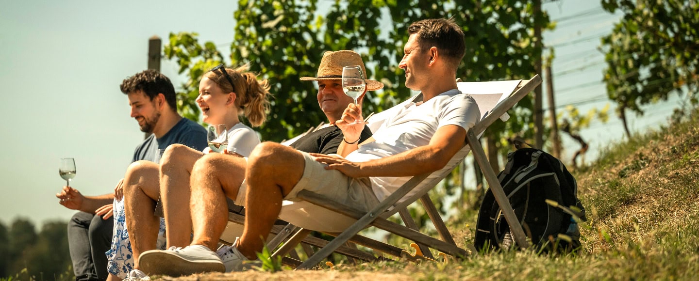 Menschen sitzen Im Liegestuhl und trinken ein Glas Wein. Und sitzen auf Liegestühlen am Weinhang.