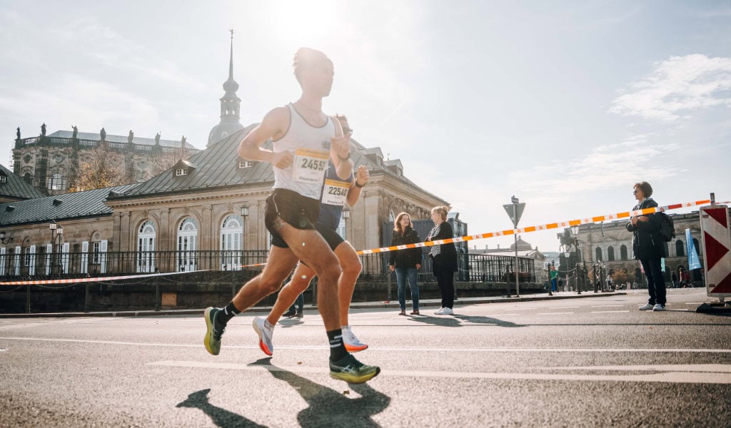 Läufer des Dresden-Marathons laufen an einem historischen Gebäude vorbei. 