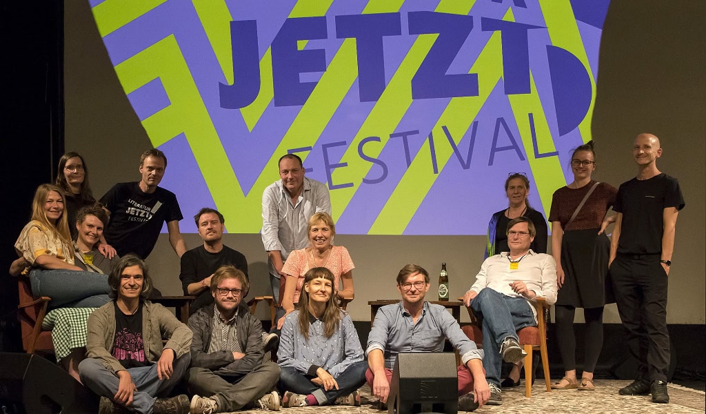 Viele Menschen sitzen vor einer Wand mit der Aufschrift "Literatur Jetzt!"