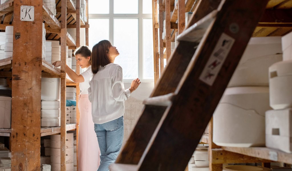 Zwei Frauen stehen im Formenarchiv der Porzellan-Manufaktur Meissen, einem Lager mit Porzellanregalen.
