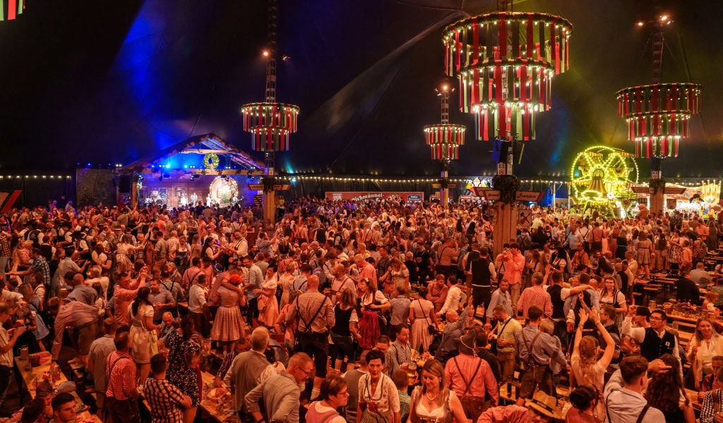 Menschen in Tracht stehen auf Bierbänken und tanzen in einem großen Festzelt.