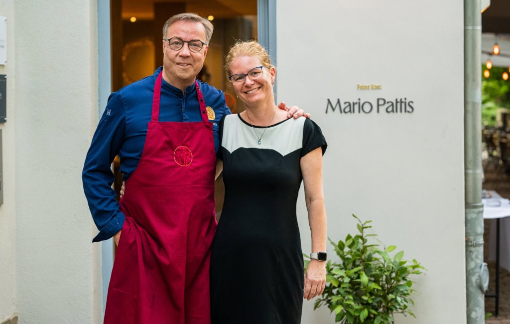 Mario Pattis und seine Frau Simona stehen vor dem Eingang des Restaurants und lächeln 