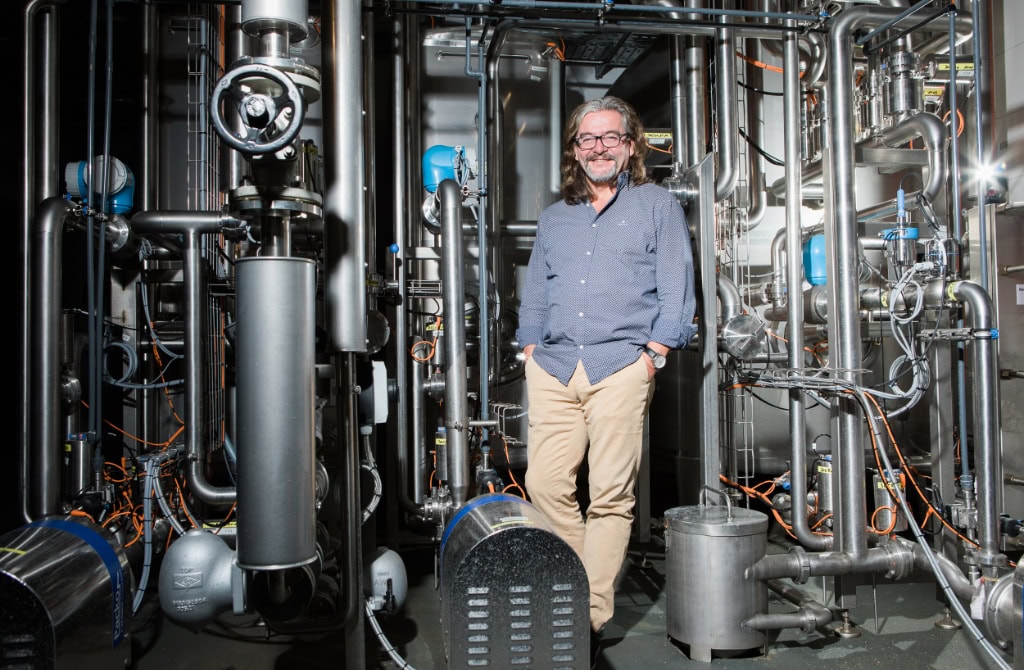 Zu sehen ist Frank Leichsenring, Mitbegründer der Dresdner Whisky Manufaktur und der Marke Hellinger 42. Er steht inmitten von Maschinen, die für die Whiskyherstellung verwendet werden.