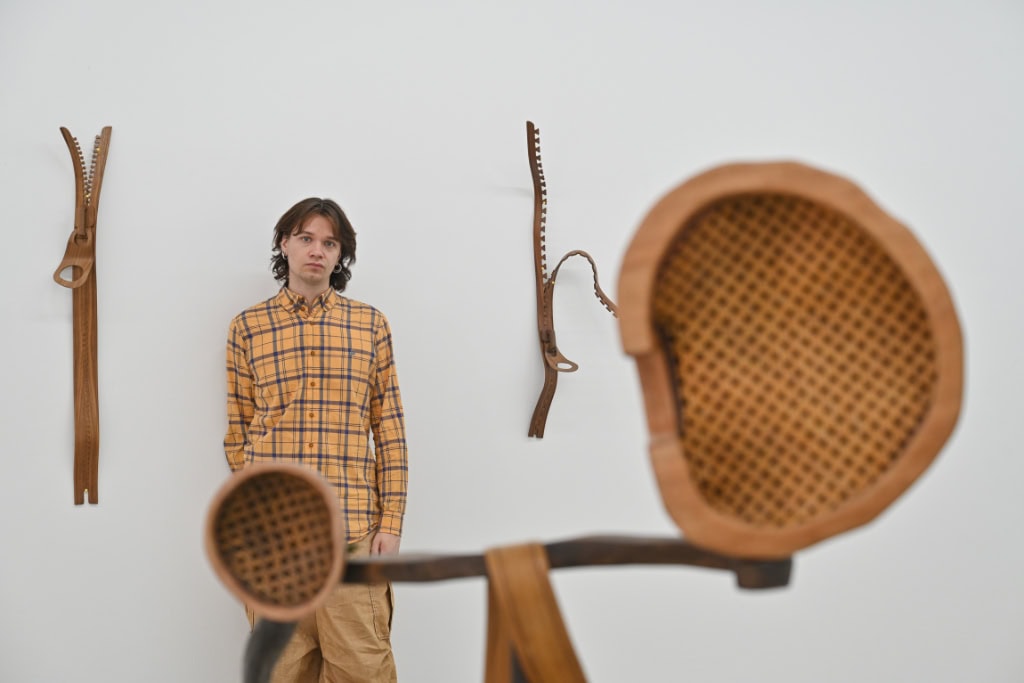 Zu sehen ist der Künstler Tobias Izsó neben seinen Werken aus Holz.