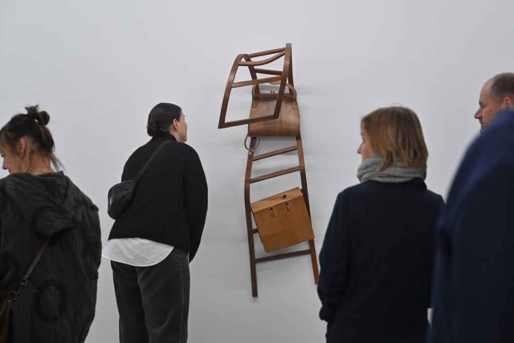 Mehrere Personen betrachten ein Kunstwerk in der Galerie im Kunstverein Dresden in Dresden-Neustadt. Dabei handelt es sich um einen ungewöhnlich verformten Holzstuhl, der an der Wand angebracht ist.