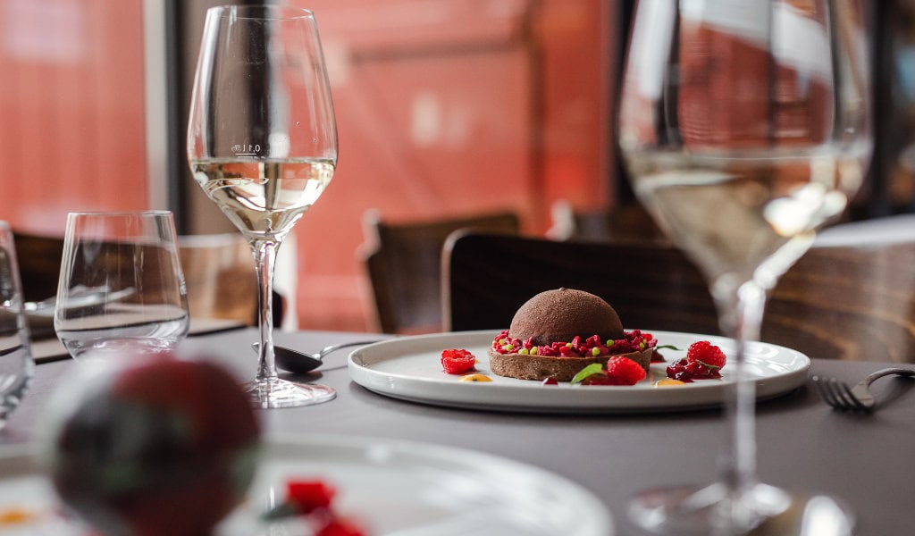 Dessert mit Schokolade, Beeren und Früchten, serviert mit zwei Gläsern Weißwein auf einem Restauranttisch