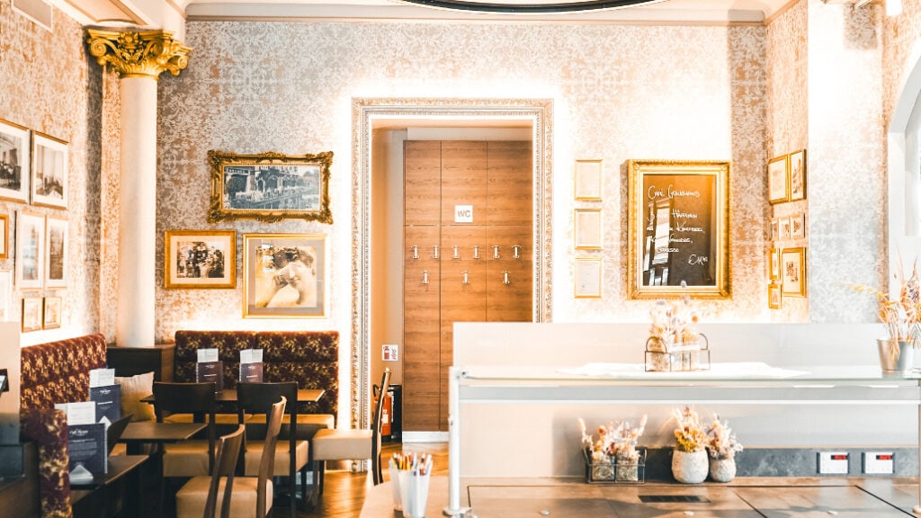 Elegantes Café mit klassischer Einrichtung, gerahmten Bildern, gemütlichen Sitzen und dekorativen Pflanzen in warmem Licht.