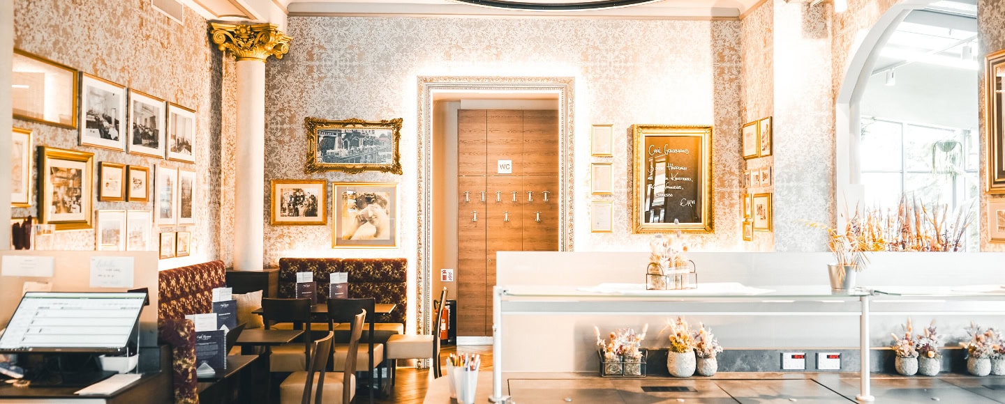 Elegantes Café mit klassischer Einrichtung, gerahmten Bildern, gemütlichen Sitzen und dekorativen Pflanzen in warmem Licht.