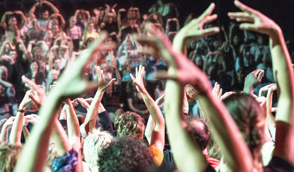 Erhobene Hände und dichtes Publikum vor Bühne, viele Personen bewegen sich gemeinsam im Rhythmus des Tanzfestivals.
