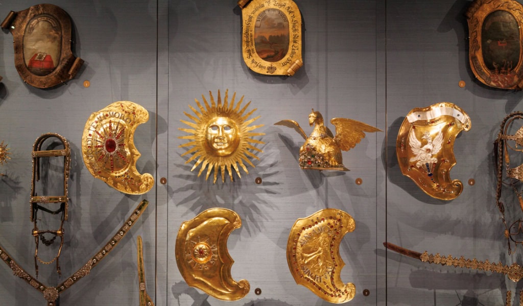 Goldene Pferdegeschirre, vergoldete Sonnenmaske und Schilde an blauer Wand, prunkvolle Rüstungsexponate in der Residenzschloss Dresden Ausstellung