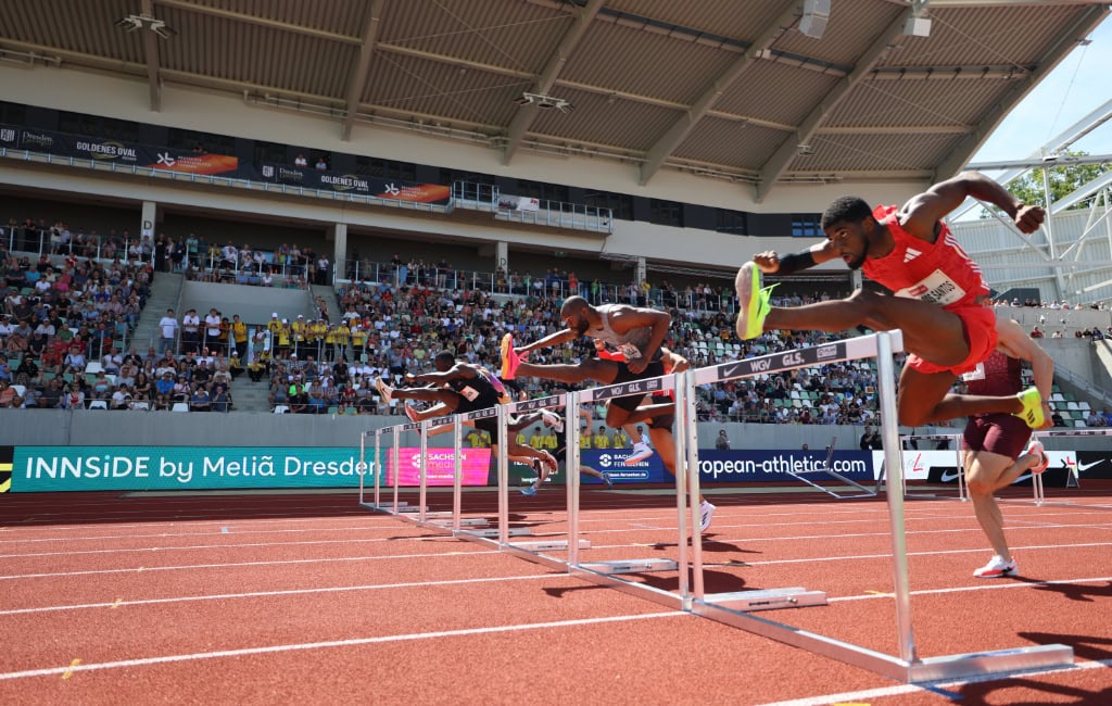 Hürdensprinter springen über Hürden auf roter Bahn im vollen Stadion beim Leichtathletikmeeting Goldenes Oval Dresden.
