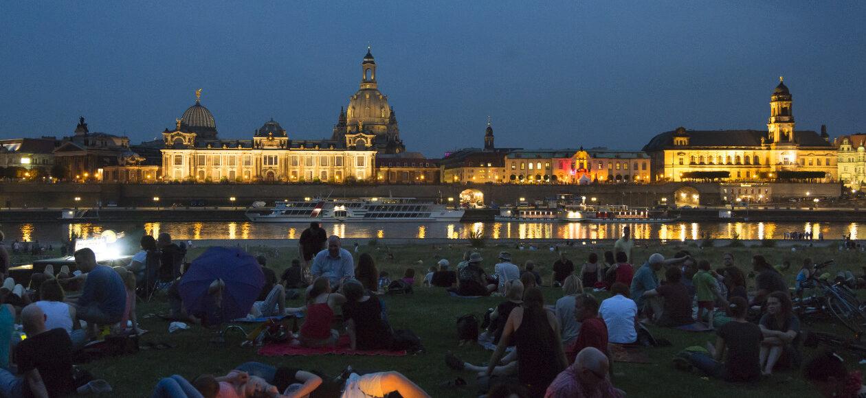 Mehrere Personen sammeln sich bei Nacht auf den Elbwiesen mit Blick aufs Wasser.