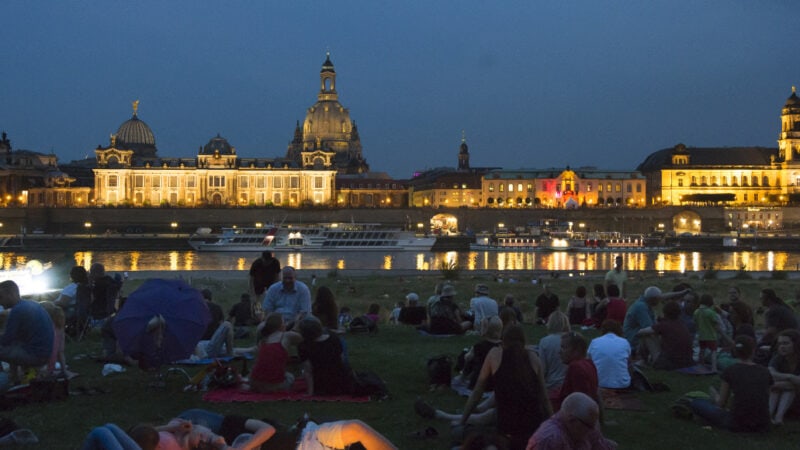 Mehrere Personen sammeln sich bei Nacht auf den Elbwiesen mit Blick aufs Wasser.
