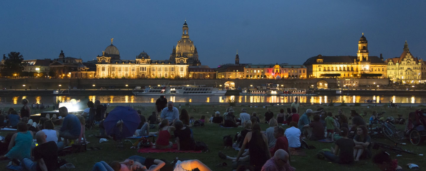 Mehrere Personen sammeln sich bei Nacht auf den Elbwiesen mit Blick aufs Wasser.