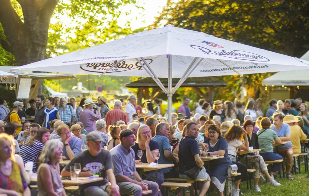 Mehrere menschen sitzen auf Bierbänken, beim Weindorf Loschwitz zum Elbhangfest in Dresden.