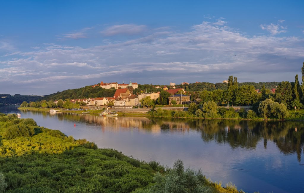 Panorama der Stadt Pirna an der Elbe mit Uferhäusern, Schlossanlage auf bewaldetem Hügel und Spiegelung im Wasser.