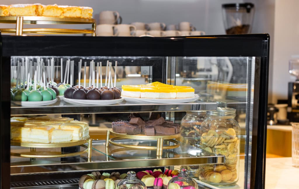 Glasvitrine im Café mit Cake Pops, Torten, Keksen und Macarons, bunte Dessertauswahl.