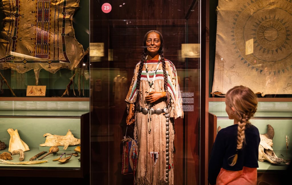 Dresden für Kinder: Ein Mädchen entdeckt im Karl-May-Museum in Radebeul eine lebensgroße Figur in traditioneller indigener Kleidung und historische Exponate.