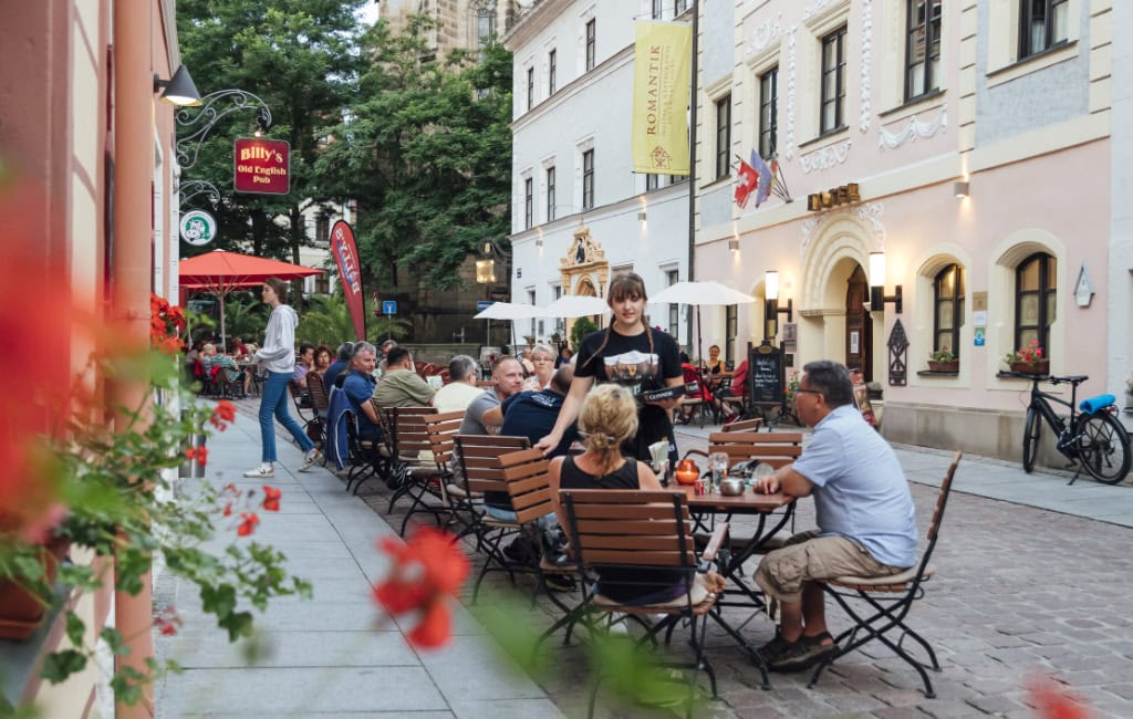 Gäste sitzen vor Restaurants und Cafés in einer Gasse der Pirnaer Altstadt.