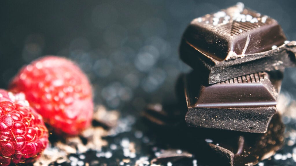 Close-up of dark chocolate pieces with fresh raspberries on a dark background.
