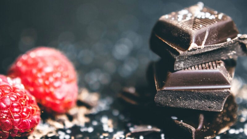Close-up of dark chocolate pieces with fresh raspberries on a dark background.
