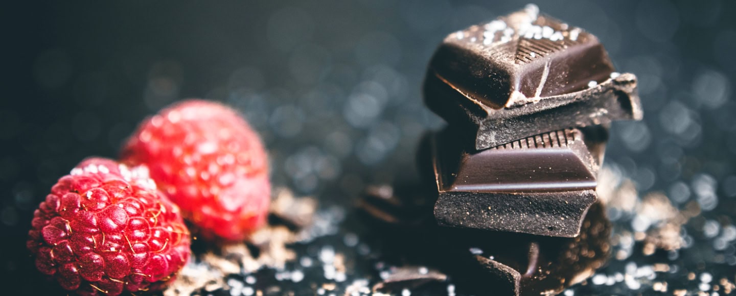 Close-up of dark chocolate pieces with fresh raspberries on a dark background.