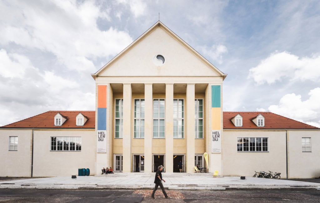 Festspielhaus Hellerau in Dresden mit markanter Säulenfassade, bunten Farbakzenten und einem Passanten im Vordergrund.