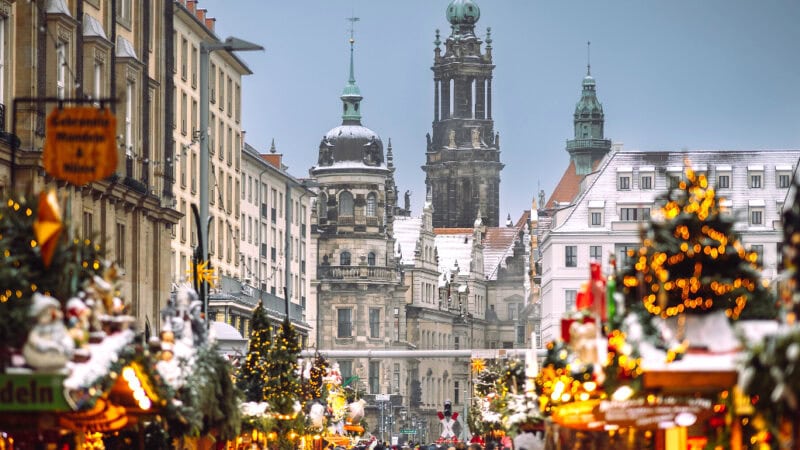Weihnachtlich geschmückter Striezelmarkt in Dresden mit beleuchteten Marktständen und Weihnachtsbäumen, im Hintergrund die Türme der Dresdner Altstadt.