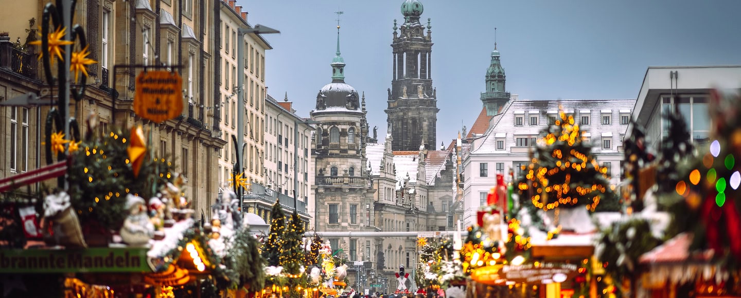 Weihnachtlich geschmückter Striezelmarkt in Dresden mit beleuchteten Marktständen und Weihnachtsbäumen, im Hintergrund die Türme der Dresdner Altstadt.