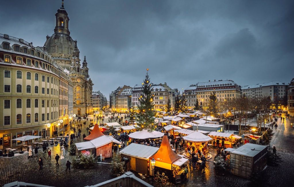 Weihnachtlich geschmückter Neumarkt in Dresden mit beleuchteten Marktständen, großem Weihnachtsbaum und der Frauenkirche im Hintergrund