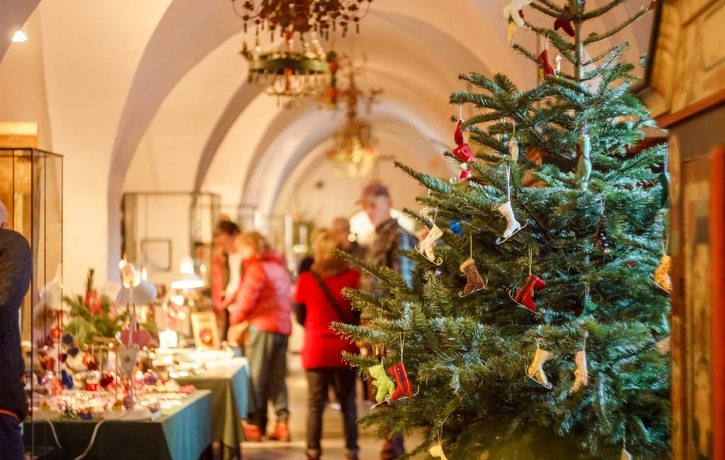 Geschmückter Weihnachtsbaum und Stände mit weihnachtlicher Volkskunst im Museum für Sächsische Volkskunst in Dresden. Besucher:innen stöbern durch die Ausstellung.