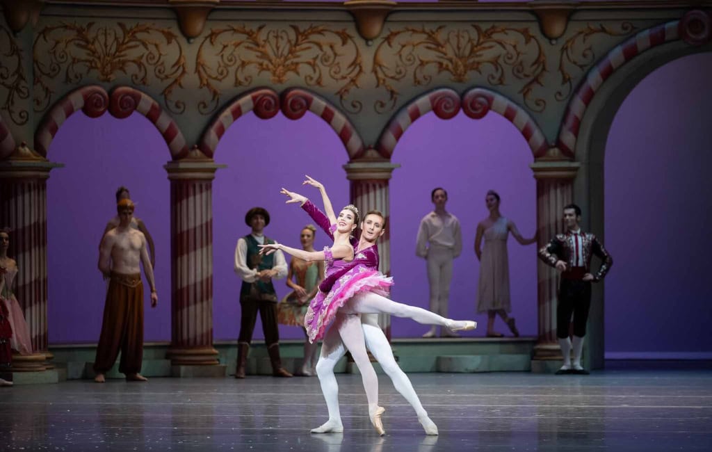 Ballettszene aus „Der Nussknacker“ in der Semperoper Dresden: Zwei Tänzer:innen in rosafarbenen Kostümen zeigen eine Hebefigur vor einer märchenhaften Bühnenkulisse.